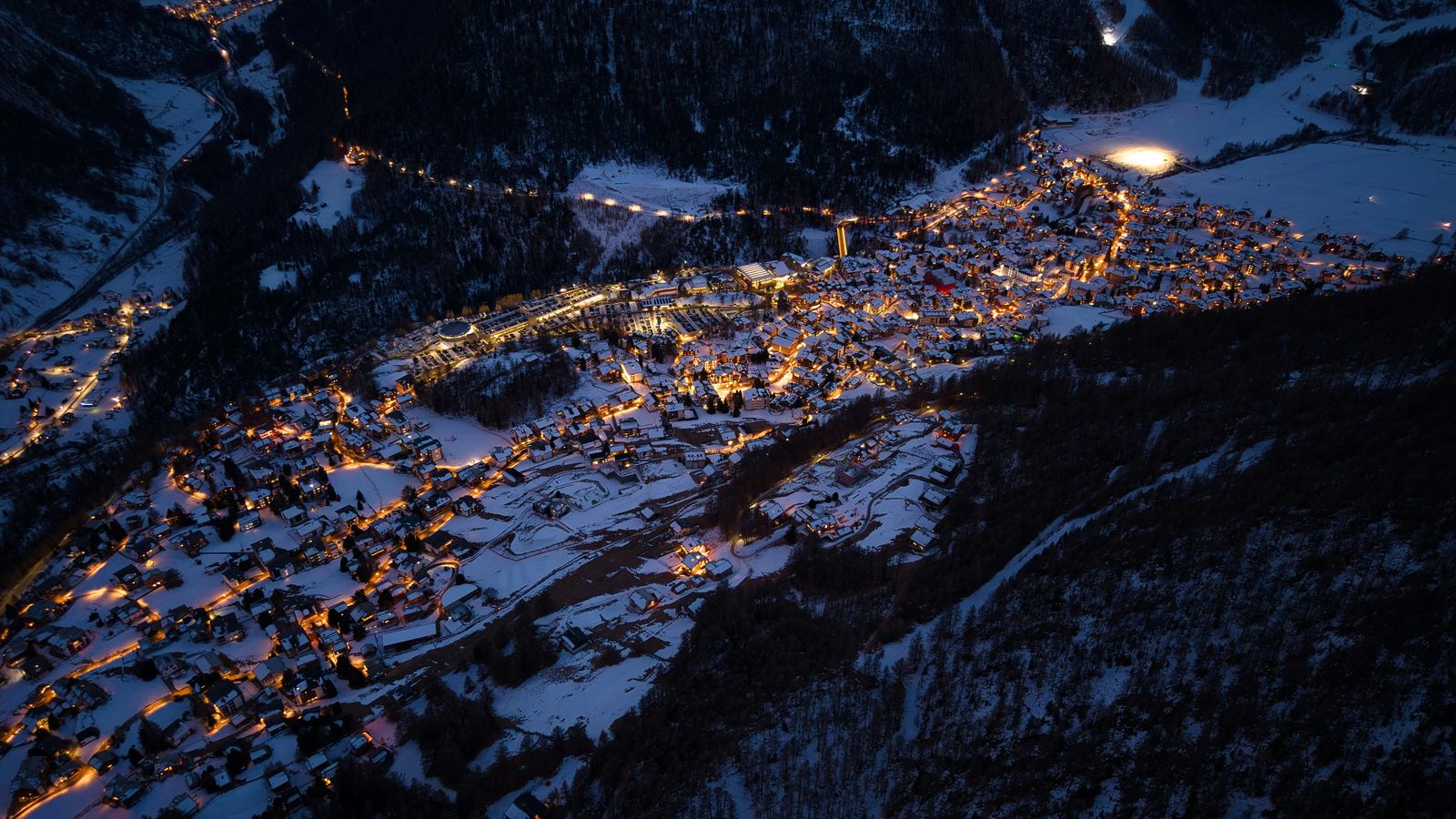 Snowy ski resort seen from above, lit up in the evening